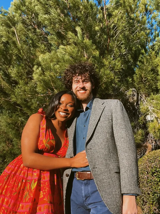 Ciera in a red dress and Cooper in a suit among the trees